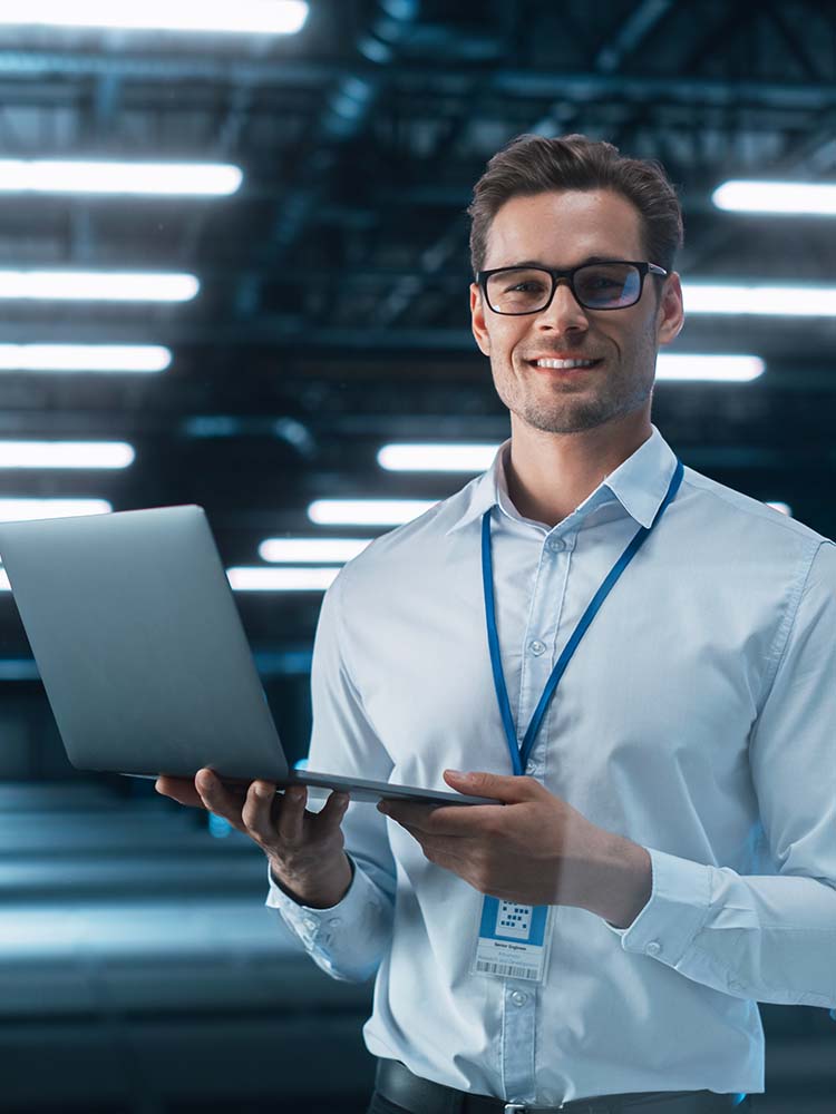 Man smiling at the camera while holding laptop.