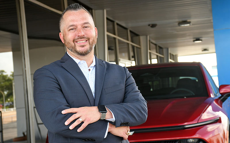 Auto tech alumnus Lenny Gordon standing in front of car at Chevrolet dealership