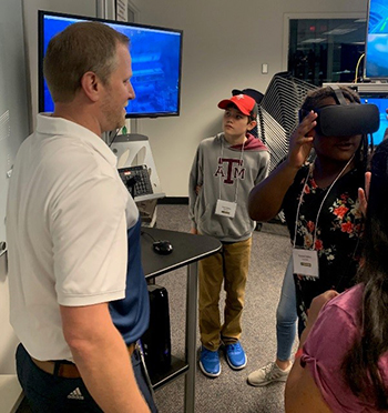 Clay Tomlinson with EnergyVenture students Elijah Hoang and Kendall Miller as they watch virtual training simulations on screen and on a virtual reality headset.